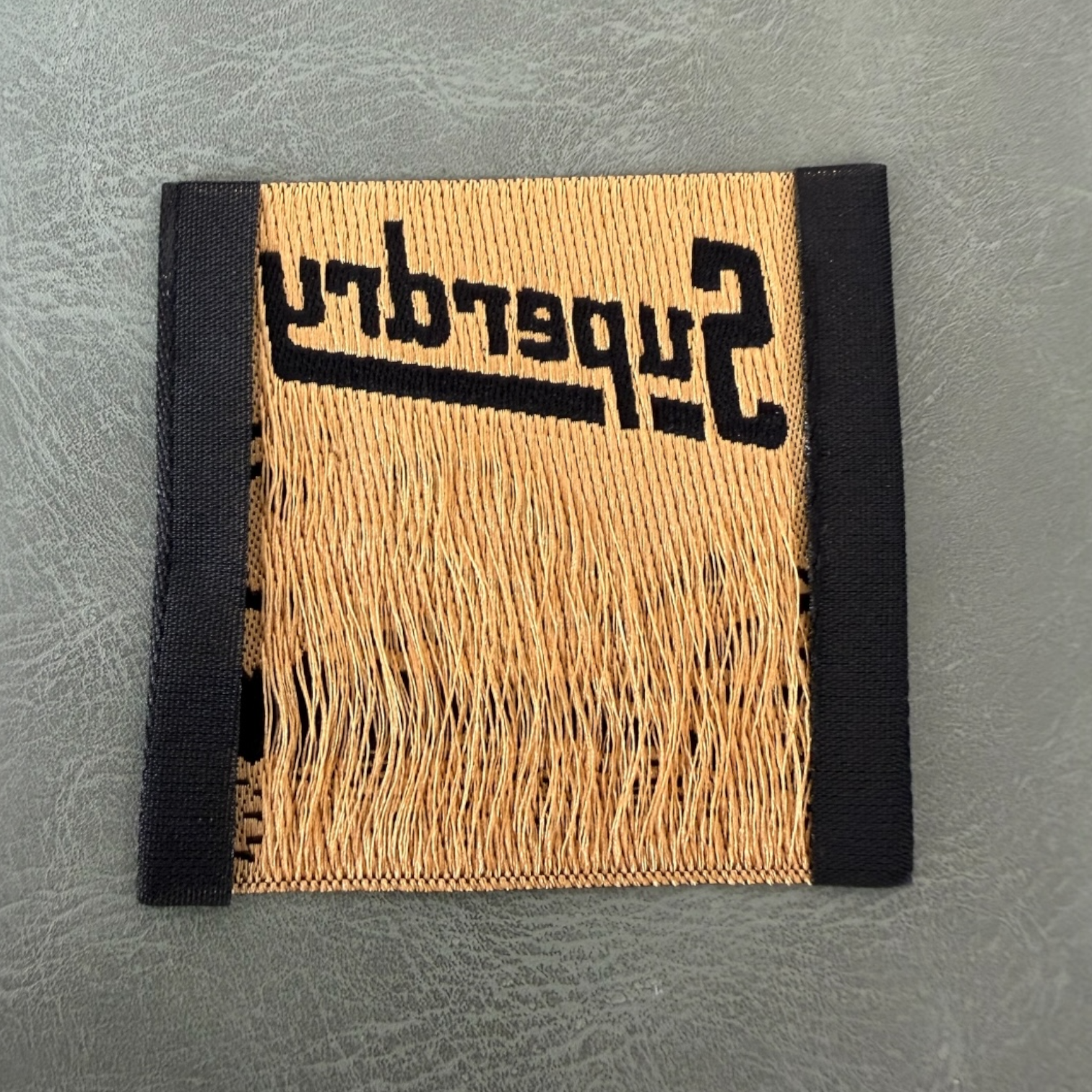 Жакардов тъкан етикет LBL 0046 5 x 5 см – черна основа със златни букви, премиум дизайн, мек стил, с лого, MOQ 1000 бр Етикети