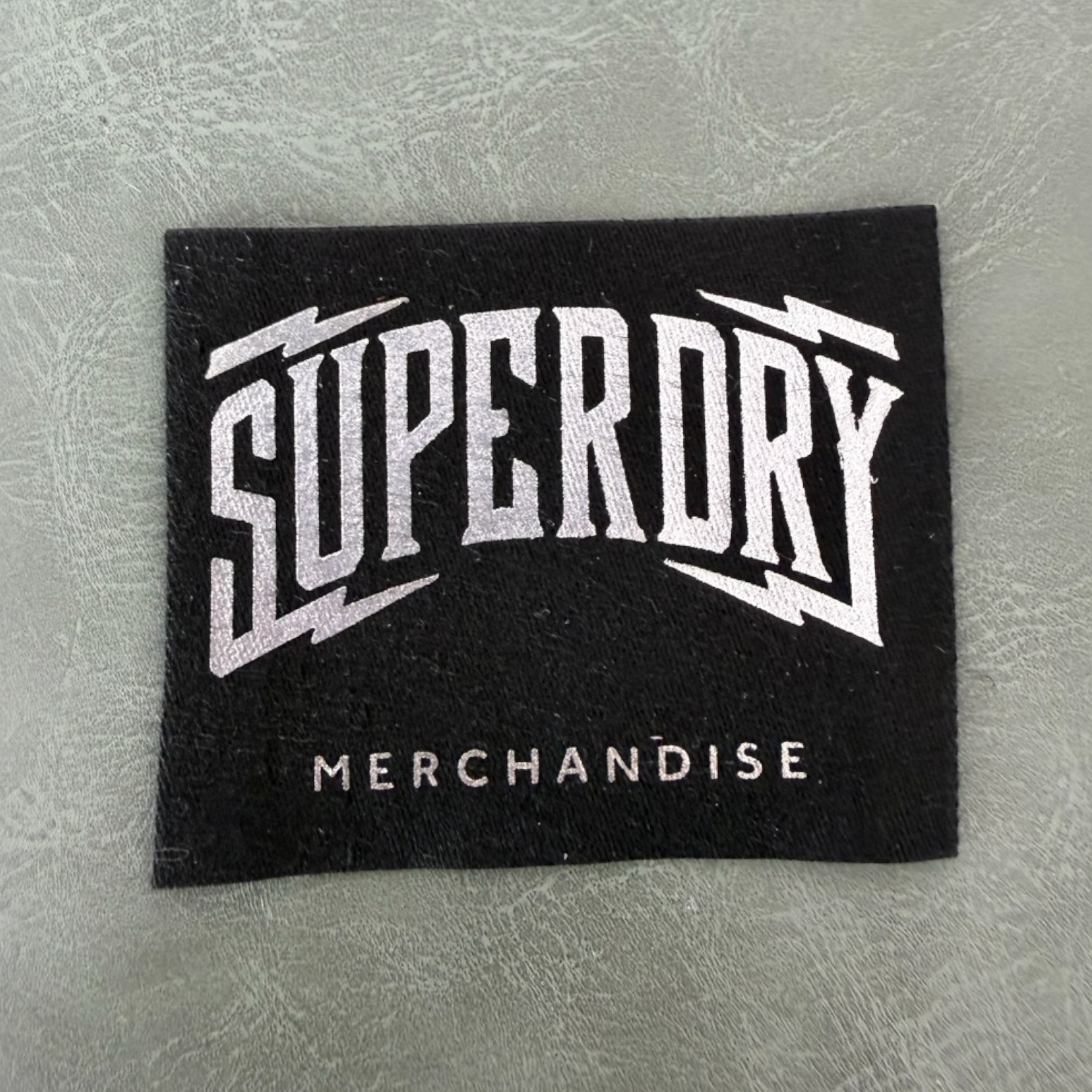 Жакардов тъкан етикет LBL 0049 5.5 x 4.5 см – черен със сребристи букви, уникален дизайн, мек премиум стил, с лого, MOQ 1000 бр Етикети