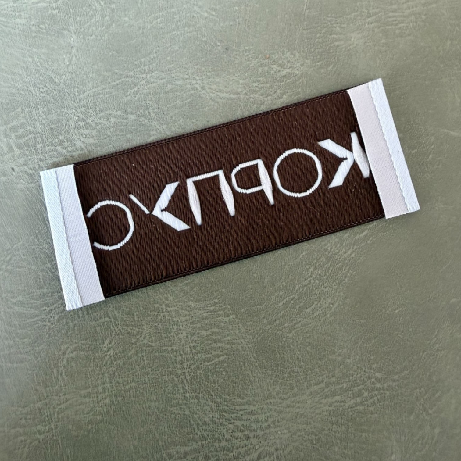 Жакардов тъкан етикет LBL 0053 6.5 x 2.5 см – тюркоаз с кафяви букви, мек премиум дизайн, с лого, MOQ 1000 бр Етикети