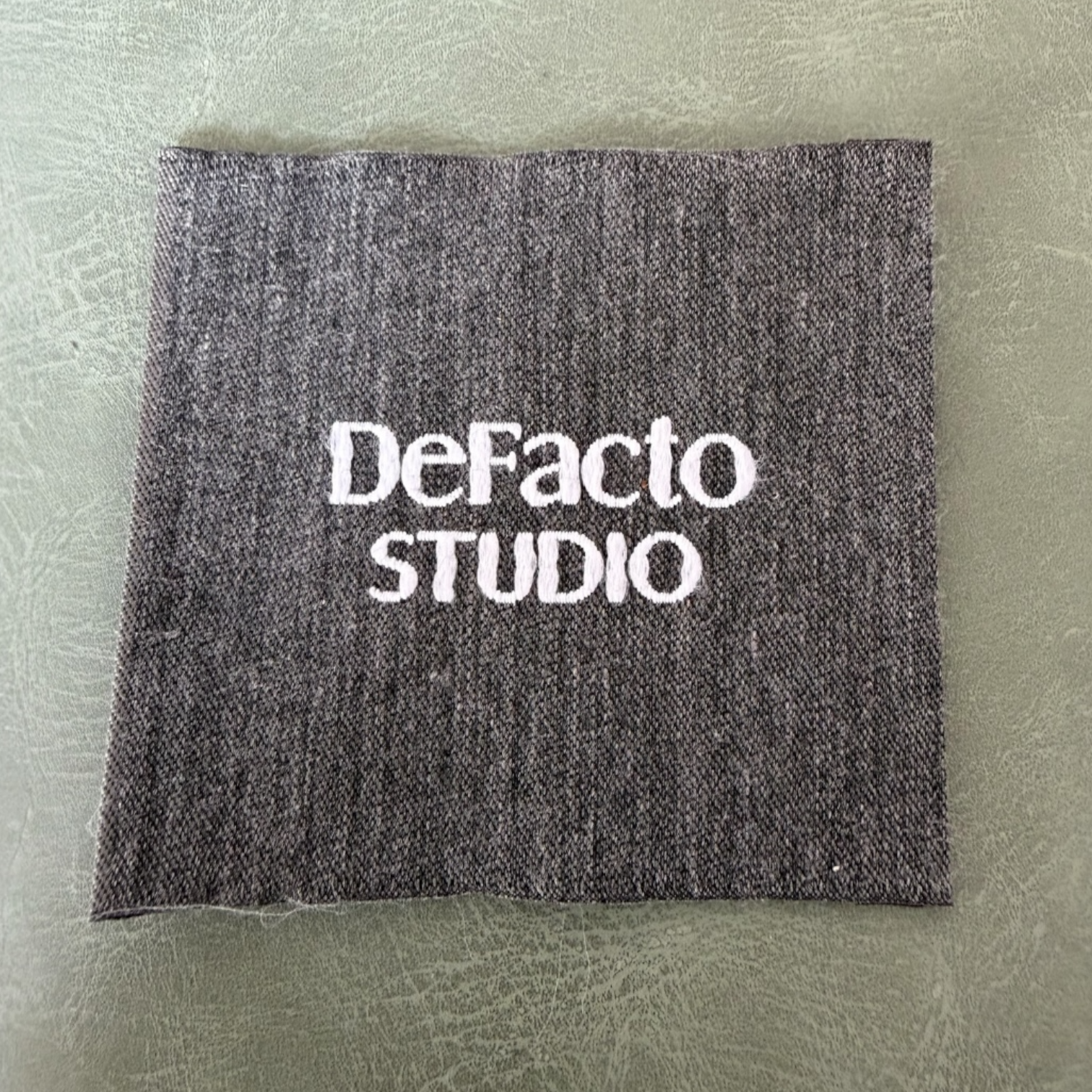 Жакардов тъкан етикет LBL 0056 6.5 x 6 см – сива основа с бели букви, мек премиум дизайн, с лого, MOQ 1000 бр Етикети