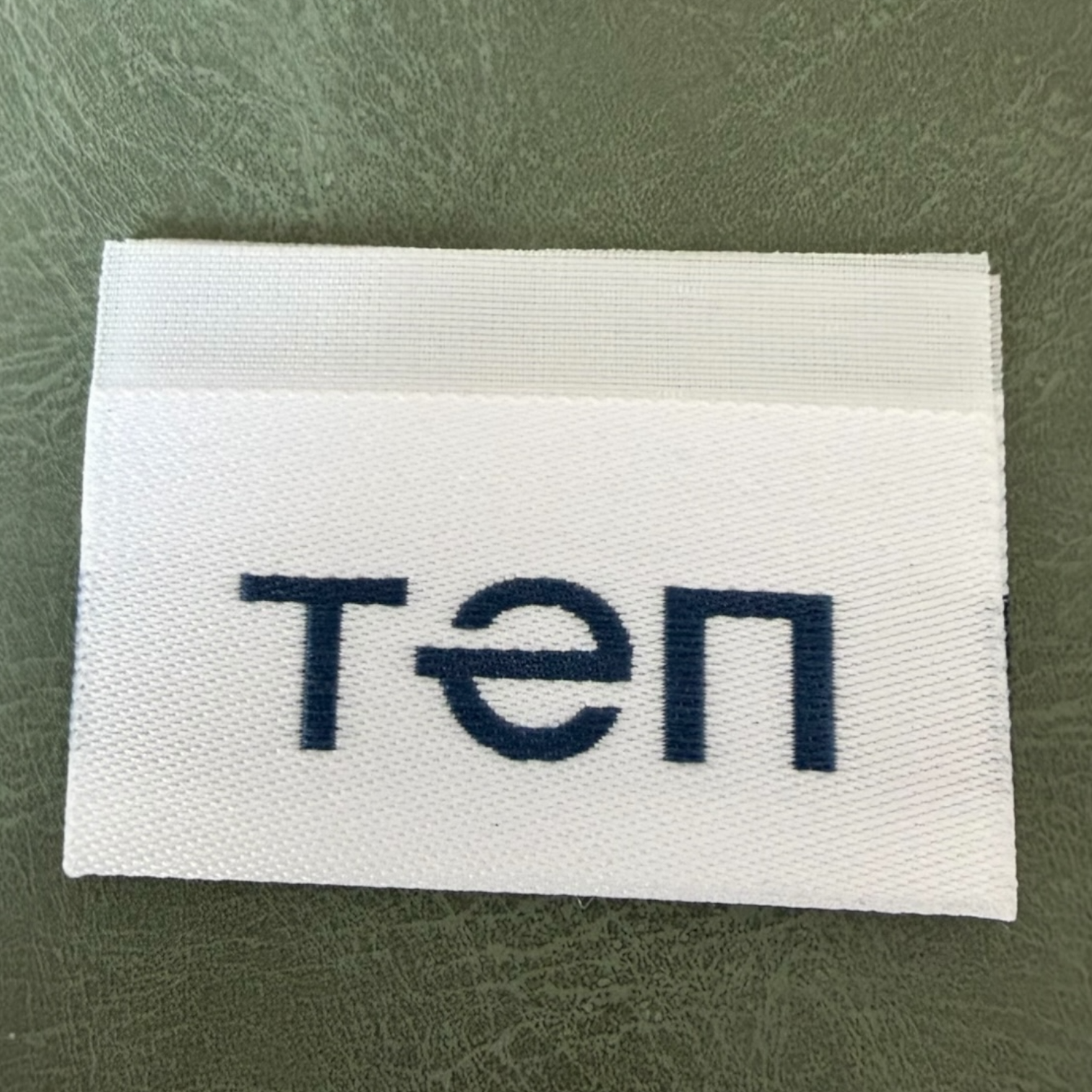 Жакардов тъкан етикет LBL 0057 5 x 4.5 см – двустранен бял със сини букви, мек премиум дизайн, с лого, MOQ 1000 бр Етикети