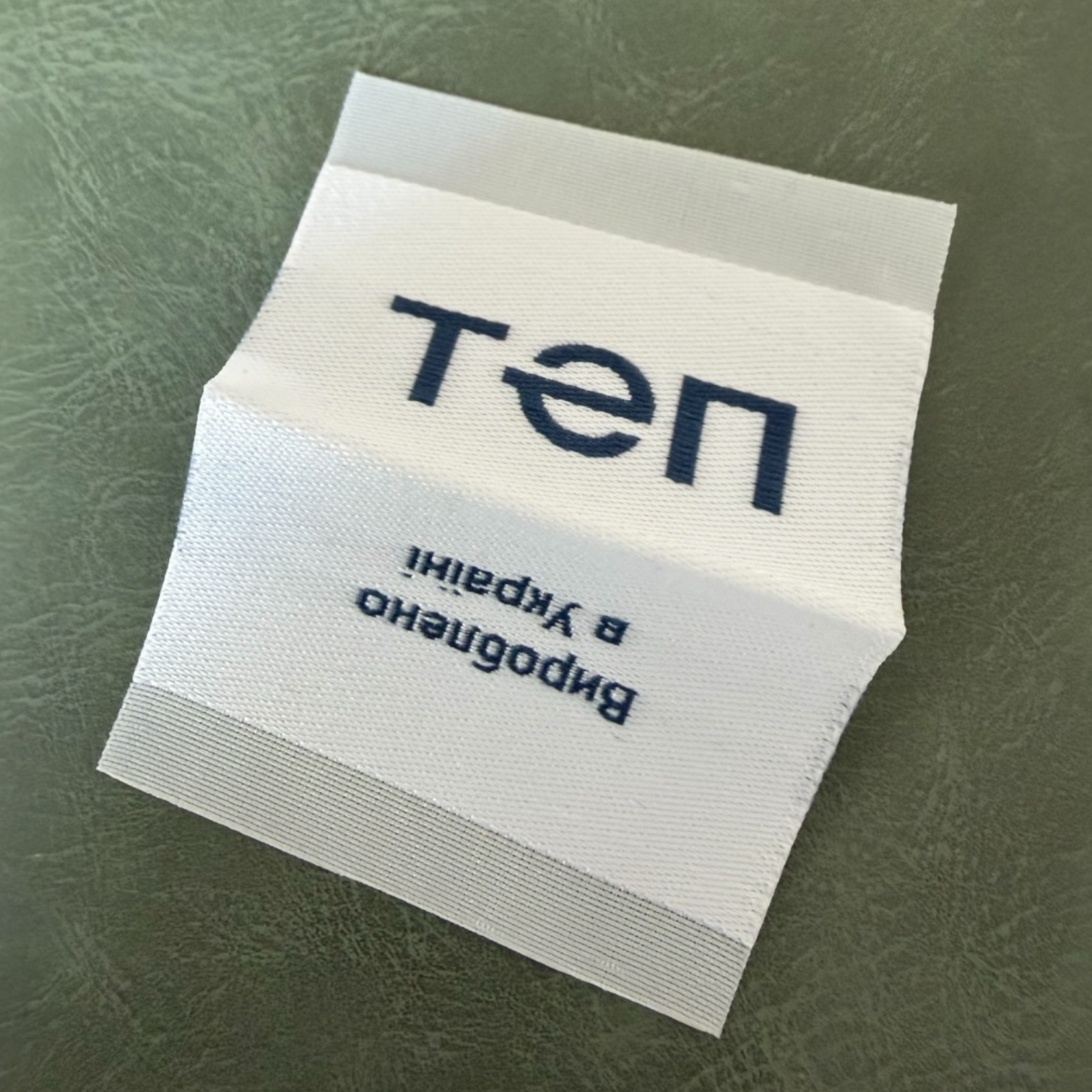 Жакардов тъкан етикет LBL 0057 5 x 4.5 см – двустранен бял със сини букви, мек премиум дизайн, с лого, MOQ 1000 бр Етикети