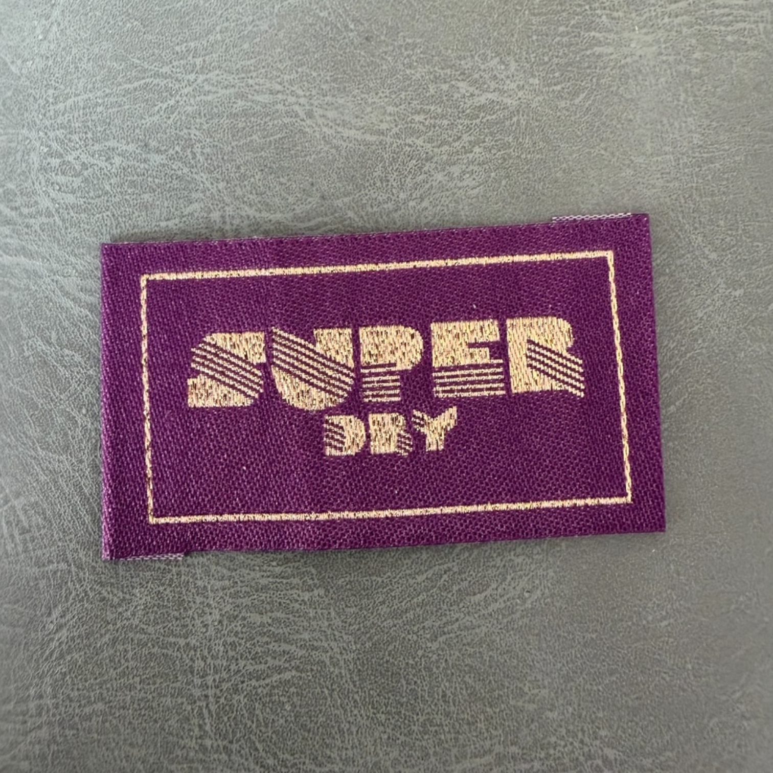 Жакардов тъкан етикет LBL 0061 5 x 2.5 см – лилава основа със златни букви, мек премиум дизайн, с лого, MOQ 1000 бр Етикети
