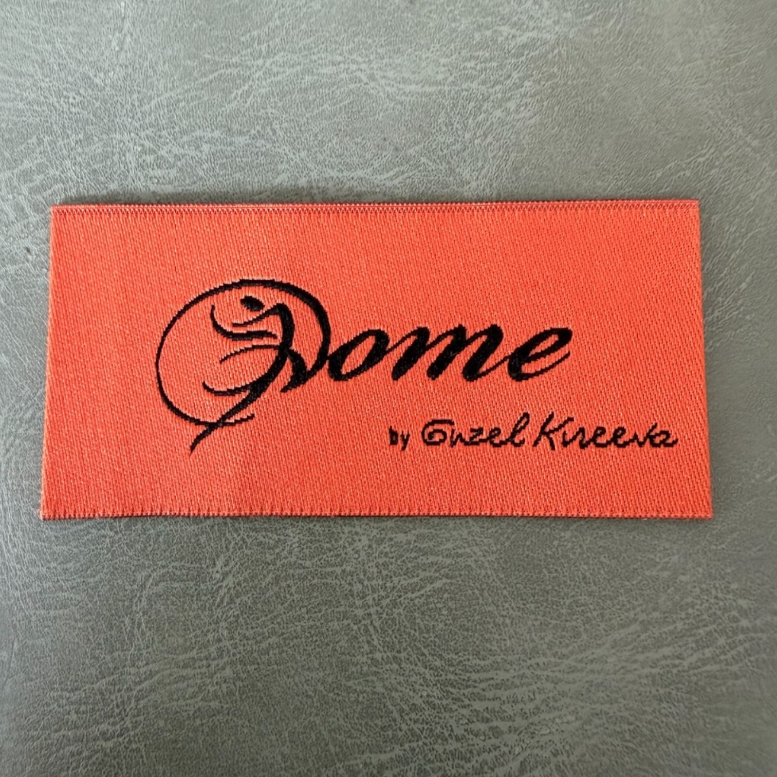 Жакардов тъкан етикет LBL 0062 6 x 3 см – оранжева основа с черни букви, мек премиум дизайн, с лого, MOQ 1000 бр Етикети