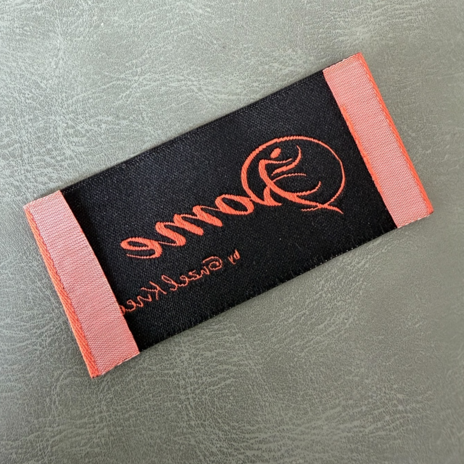 Жакардов тъкан етикет LBL 0062 6 x 3 см – оранжева основа с черни букви, мек премиум дизайн, с лого, MOQ 1000 бр Етикети